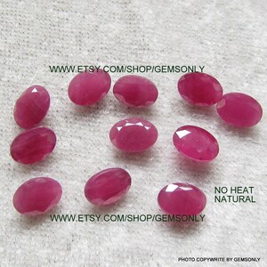 May include: A collection of oval-shaped, natural ruby gemstones in varying shades of pink and red. The gems are faceted, displaying multiple reflective surfaces. The image includes the text "NO HEAT NATURAL" and a website address.