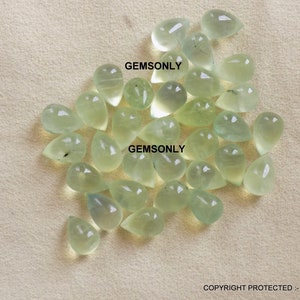 May include: A collection of pale green, teardrop-shaped gemstones. The gems are translucent and appear to be polished, with a slight variation in color. The image includes the text "GEMSONLY" in multiple places.