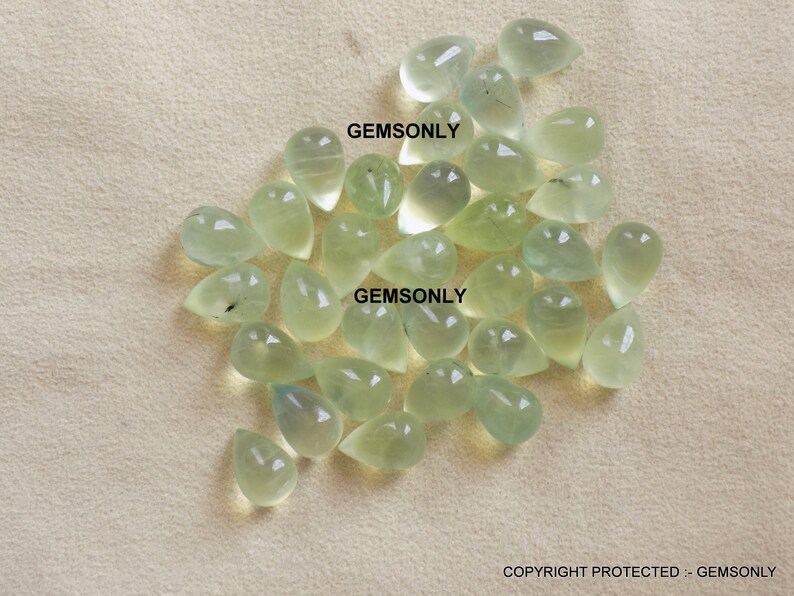 May include: A collection of pale green, teardrop-shaped gemstones. The gems are translucent and appear to be polished, with a slight variation in color. The image includes the text "GEMSONLY" in multiple places.