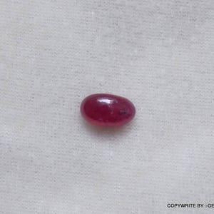 Puede incluir: Primer plano de una piedra preciosa roja de forma ovalada sobre un fondo blanco.