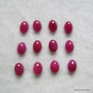 May include: Twelve oval-shaped, deep red gemstones. The gemstones are arranged in three rows of four.