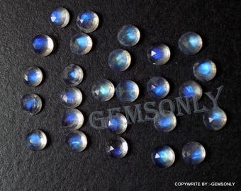 May include: A collection of 20 iridescent moonstone gemstones, each with a unique blue sheen. The stones are faceted and have a round shape. They are arranged on a black surface.