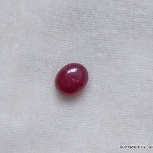 Peut inclure: Gros plan sur une pierre précieuse rouge de forme ovale. La pierre précieuse est lisse et polie, avec un léger éclat.