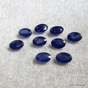 Może przedstawiać: Dziesięć owalnych niebieskich szafirów, każdy o nieco innym odcieniu niebieskiego, ułożonych jest w kółko na białym tle.