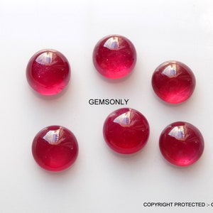 May include: Six round, red ruby cabochons, each with a smooth, polished surface.  GEMSONLY is printed in white text on a white background.