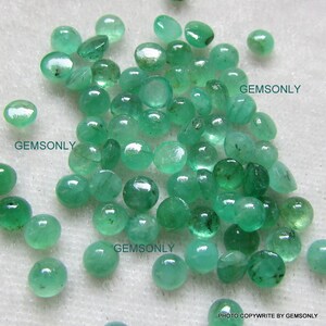 May include: A collection of round, green emerald gemstones. The gemstones are smooth and polished, with a slight shine. The gemstones are arranged in a pile, with some overlapping. The text "GEMSONLY" appears three times in the image.