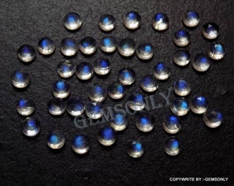 May include: A collection of iridescent moonstone cabochons in various sizes. The stones are a milky white with a blue sheen. The stones are arranged on a black surface.