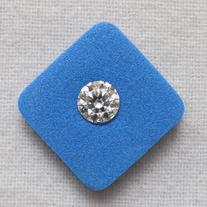 May include: A round-cut diamond with multiple facets, set against a bright blue square. The diamond sparkles, reflecting light. The blue square is a contrasting backdrop, highlighting the diamond's brilliance. This image showcases a gemstone.
