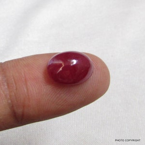 May include: A cabochon cut ruby gemstone with a deep red color. The gemstone is smooth and polished, with a slight sheen.