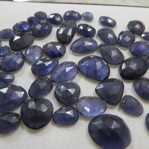 Peut inclure: Une collection de pierres précieuses facettées bleu foncé. Les pierres sont de forme ovale et de tailles variées.