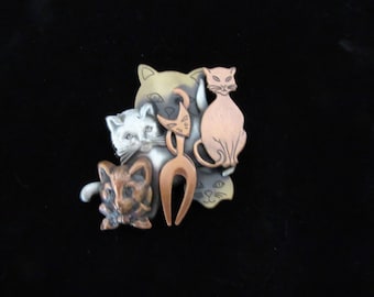 May include: A cluster of five metal cat figurines in various poses. The cats are made of copper and silver toned metal and are arranged in a group.