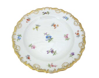 May include: White porcelain plate with a gold scalloped rim and delicate floral designs in various colors. The plate features small, hand-painted flowers scattered across the surface, creating an elegant and classic aesthetic.