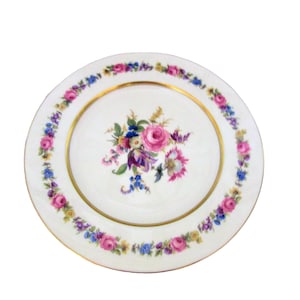 May include: A white ceramic dinner plate with a gold rim and a floral design. The flowers are pink, purple, and white, and they are arranged in a bouquet in the center of the plate.
