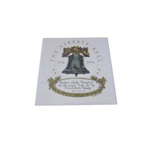 May include: A white square decorative item with an illustration of the Liberty Bell. The text includes "THE LIBERTY BELL 1776 1976" and a quote: "Proclaim Liberty Throughout all the Land Unto all The Inhabitants Thereof."