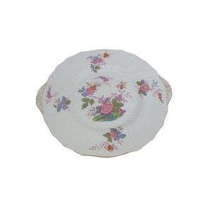 May include: White, scalloped-edge serving plate with a floral design. The plate features a central arrangement of pink, blue, and purple flowers, with additional floral clusters around the rim. Gold accents are visible on the handles.