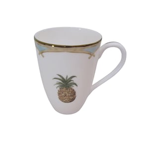 May include: White ceramic mug with a gold rim and a pineapple illustration. The mug features a curved handle and a decorative band with blue accents near the rim. The pineapple is brown and green.