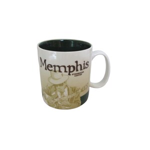 May include: A white ceramic mug with a green interior and a brown graphic of a man playing a guitar. The mug has the text "Memphis Starbucks Coffee" printed on it.