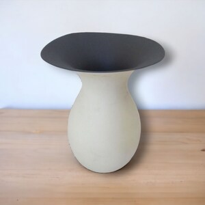 May include: A white ceramic vase with a wide, black, flared opening. The vase has a rounded, bulbous body.