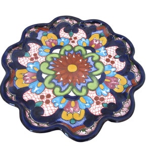 May include: A colorful ceramic plate with a floral design. The plate is blue, green, yellow, pink, and red. It has a scalloped edge.