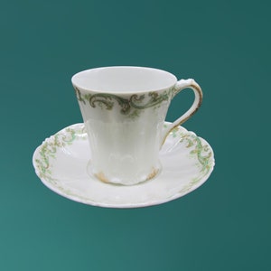 May include: A white teacup and saucer with a green and gold floral design.