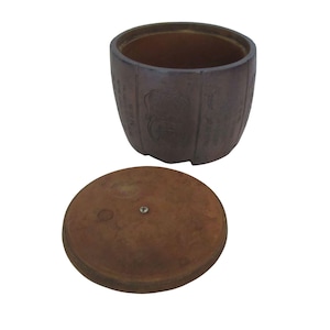 May include: A brown ceramic container with a matching lid. The container has a cylindrical shape with vertical grooves and embossed designs. The lid is round with a small metal knob in the center. The items are set against a white background.