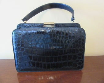 May include: A black crocodile-embossed leather handbag with a top handle and a gold clasp.