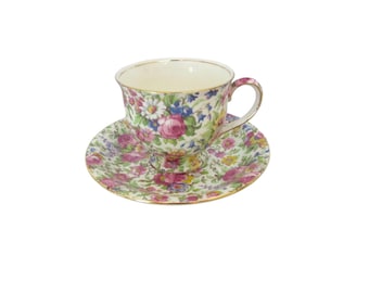 May include: A vintage floral teacup and saucer set with a white background and a colorful floral pattern. The cup has a gold rim and the saucer has a gold trim.