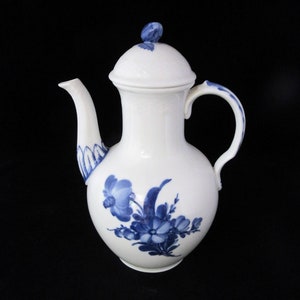 May include: A white ceramic coffee pot with a blue floral design. The pot has a round body, a spout, a handle, and a lid.
