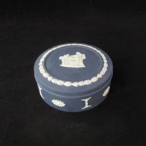 May include: A round blue and white ceramic trinket box with a white design on the lid. The design features a group of figures in a classical style.