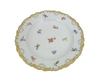 May include: White porcelain plate with a gold scalloped rim and delicate floral designs. The plate features small, colorful flowers scattered across the surface, creating an elegant and vintage aesthetic. A classic piece for serving or display.