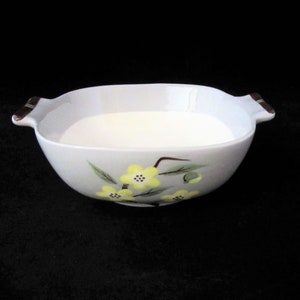 May include: White ceramic serving bowl with two brown handles and a floral design featuring yellow flowers and green leaves.