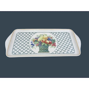 May include: Rectangular serving tray with a white background and a green trellis pattern. A central circular design features a basket overflowing with colorful fruits. The tray has gold trim and integrated handles.