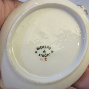 May include: White porcelain saucer with a green and gold rim. The bottom of the saucer has a green mark that reads "Richard Ginori L2".