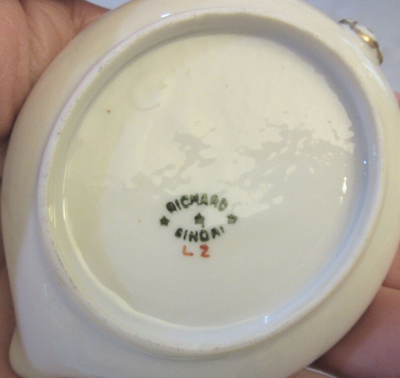 May include: White porcelain saucer with a green and gold rim. The bottom of the saucer has a green mark that reads "Richard Ginori L2".