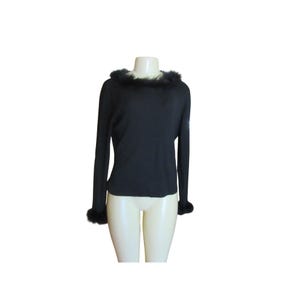 May include: A black long-sleeve sweater with fur trim around the neckline and cuffs. The sweater is displayed on a mannequin against a white background. The fur appears to be dark in color.