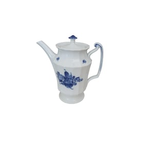 May include: White porcelain teapot with blue floral decoration. The teapot features a lid with a blue finial, a curved handle, and a spout. The floral design is concentrated on the front. The teapot sits on a small pedestal base.