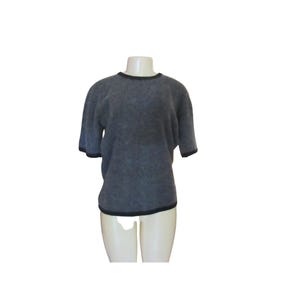 May include: A grey short-sleeved sweater with black trim around the neckline and sleeves. The sweater is displayed on a mannequin against a white background. The fabric appears soft and textured.