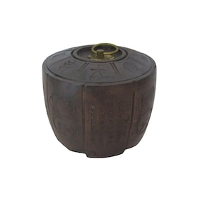 May include: A brown, antique-style container with a lid and a brass handle. The container has etched designs and text in an Asian language. The container is cylindrical with a rounded top and bottom.