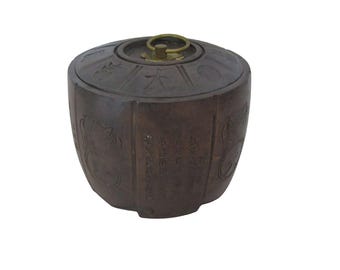 May include: A brown, antique-style container with a lid and a brass handle. The container has etched designs and text in an Asian language. The container is cylindrical with a rounded top and bottom.