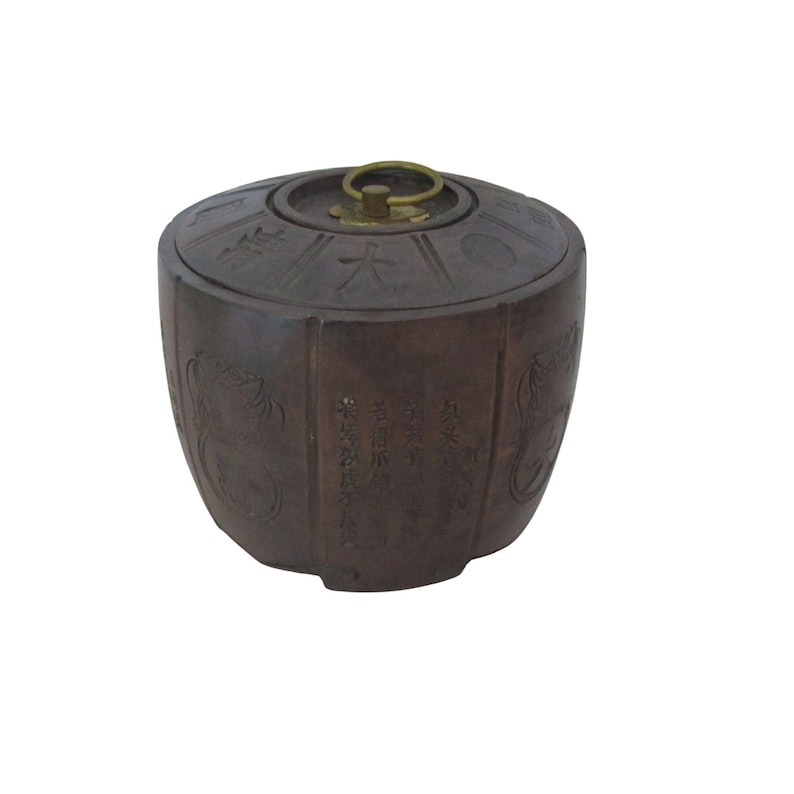 May include: A brown, antique-style container with a lid and a brass handle. The container has etched designs and text in an Asian language. The container is cylindrical with a rounded top and bottom.