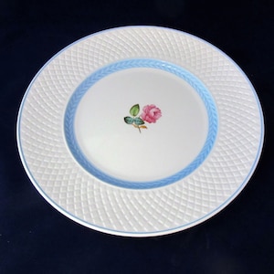 May include: White ceramic dinner plate with a blue and white woven border and a single pink rose painted in the center.