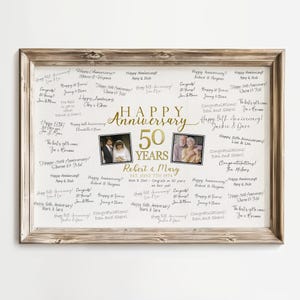 May include: A framed anniversary sign with the words "Happy Anniversary 50 Years" in gold lettering. The sign includes two small photos and handwritten messages. The frame is a light brown color.