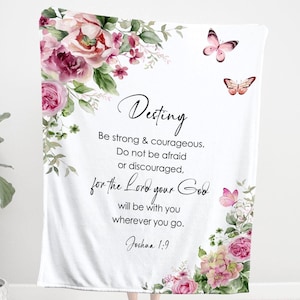 Puede incluir: Manta blanca con diseños florales y mariposas. La manta presenta la palabra "Destiny" y un versículo bíblico: "Sé fuerte y valiente...porque el Señor tu Dios estará contigo dondequiera que vayas. Josué 1:9."