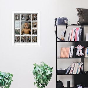 May include: A white picture frame with 12 openings for photos. Each opening has a white border and a label for each month of the year. The frame is hanging on a white wall. The name "Logan" is written in the center of the frame.