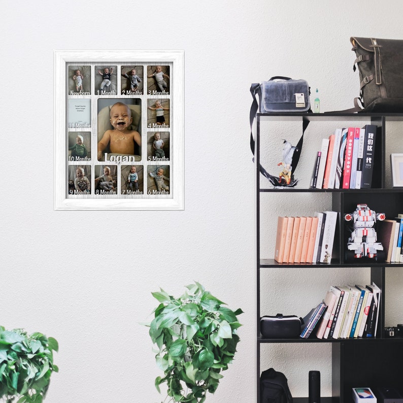 May include: A white picture frame with 12 openings for photos. Each opening has a white border and a label for each month of the year. The frame is hanging on a white wall. The name "Logan" is written in the center of the frame.