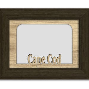 May include: A brown wooden picture frame with a cutout of the words "Cape Cod" in the center. The frame has a light brown wood inner border.