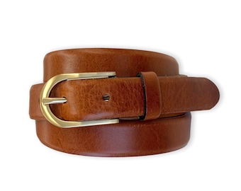 Peut inclure: Une ceinture en cuir marron enroulée avec une surface texturée et une boucle en métal doré poli. La ceinture comprend un passant en cuir assorti et un trou de réglage visible, présentant un design classique aux bords lisses.