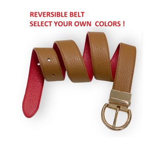 Peut inclure: Une ceinture réversible avec un extérieur beige texturé et un intérieur rouge vif, dotée d'une boucle en métal doré. Le texte REVERSIBLE BELT SELECT YOUR OWN COLORS ! est affiché au-dessus de la ceinture enroulée avec des trous de réglage.