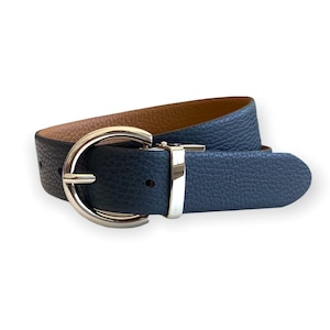 Pode incluir: Um cinto reversível com um exterior azul-marinho texturizado e um interior castanho-claro liso. O cinto é preso com uma fivela de metal prateado polido que tem uma estrutura arredondada semicircular e um passador de metal a condizer.