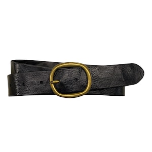 Puede incluir: Un cinturón negro con superficie texturizada y una hebilla metálica redondeada en tono latón antiguo. El cinturón presenta una serie de agujeros preperforados a lo largo de la tira, la cual se pasa por la hebilla para asegurar el cierre horizontal.